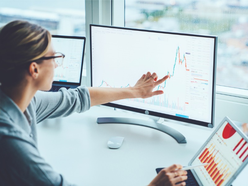 Une femme d'affaires étudie les marchés financiers pour calculer les risques et les bénéfices possibles. L'argent de comptabilité d'économiste féminin avec des graphiques de statistiques pointant sur l'écran de l'ordinateur au bureau.