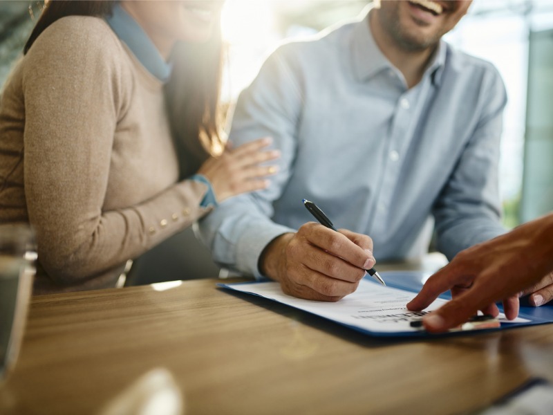 Gros plan d’un couple méconnaissable signant un contrat au bureau.