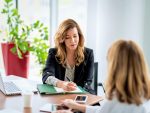 Femme d'affaire à un bureau, écrivant sur un document alors qu'elle parle avec une autre femme.