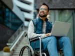 Homme handicapé avec ordinateur portable en fauteuil roulant à l’extérieur.