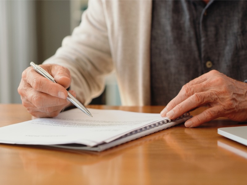 es mains d’un homme de pension lisent des documents de retraite sur la police, les options de placement et la couverture funéraire tout en planifiant les finances, les assurances et le budget à la maison. Signature du testament, du document juridique