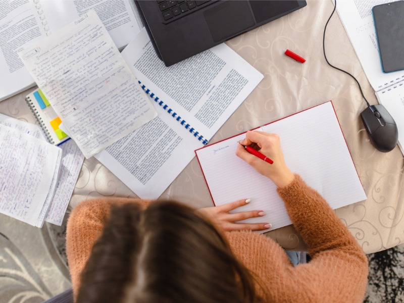 Une femme assise à une table devant un ordinateur avec pleins de documents autour d'elle.