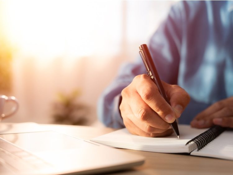 lan rapproché de la main d’homme utilisant la note de plume d’écriture sur le papier ou la lettre de cahier, journal sur le bureau de bureau de table. Lieu de travail pour étudiant, écrivain avec espace de copie.