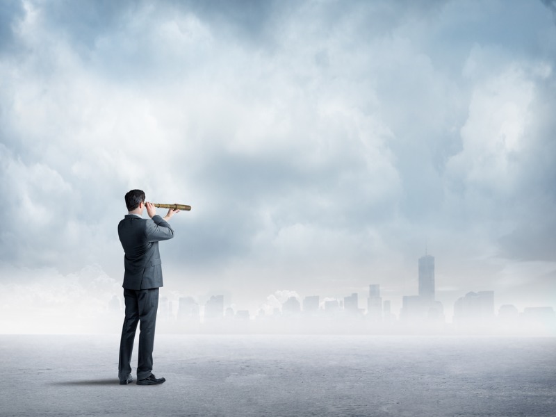 Un homme d’affaires regarde vers la ville à l’horizon à travers une longue-vue.