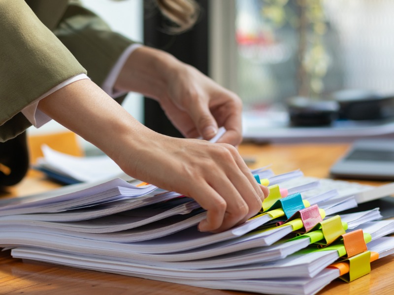 La secrétaire fouille dans une pile de documents importants sur la table du bureau, les livre au gestionnaire pour qu’il les présente à temps lors de la réunion. Notion de difficulté à trouver de l’information à partir de piles de documents.